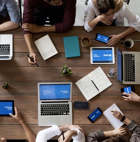Birds-eye view of a collaborative gathering of people working on laptops and tablets.