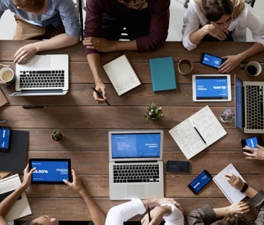 Birds-eye view of a collaborative gathering of people working on laptops and tablets.